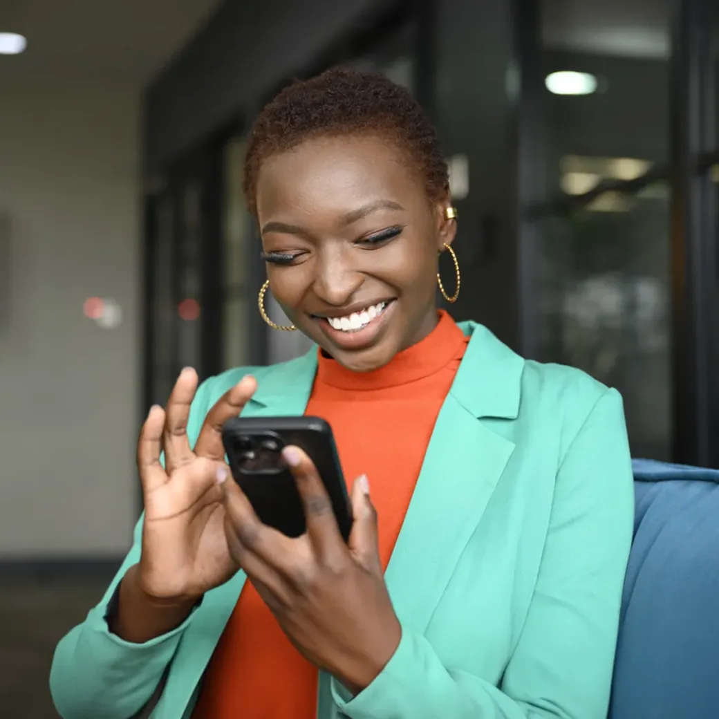 business-professional-using-smart-phone-1644128335 Waist-up view of shorthaired woman wearing hoop earrings, teal jacket over orange top, and smiling while scrolling portable device in modern office.