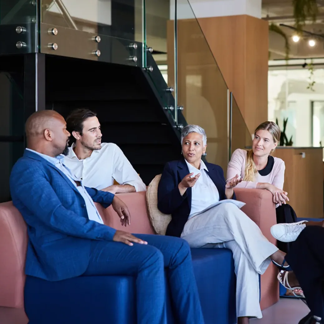 businesspeople-smiling-during-a-meeting-1397882830 Diverse group of smiling businesspeople talking together during a casual meeting in the lounge area of a modern office