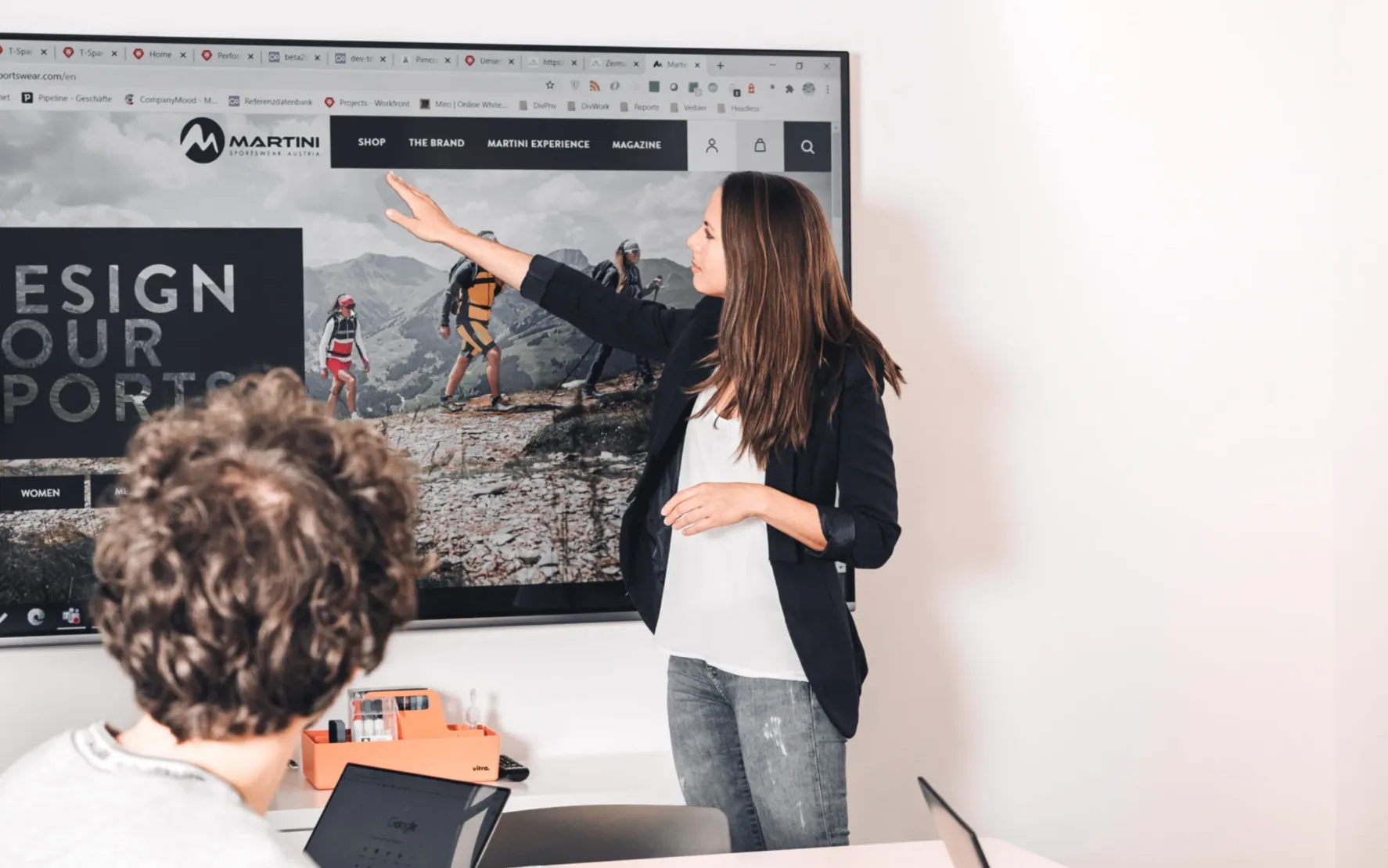 Digitalisierung im Tourismus ist unsere Leidenschaft: valantic austria Foto von einer jungen Frau, die vor ihren Kollegen von valantic Austria eine Präsentation über Digital Travel hält.