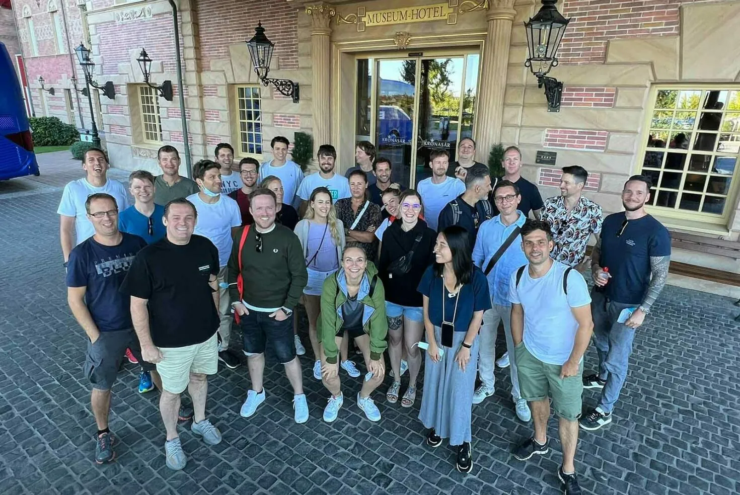 Eine Gruppe von Menschen posiert gemeinsam vor dem Museum Hotel. Die Gruppe besteht aus Männern und Frauen, leger gekleidet, die in die Kamera lächeln.