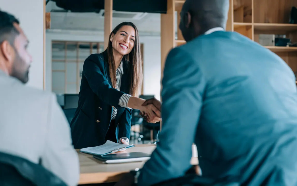 successful-partnership-1365436662 Business people shaking hands in the office. Group of business persons in business meeting. Three entrepreneurs on meeting in board room.