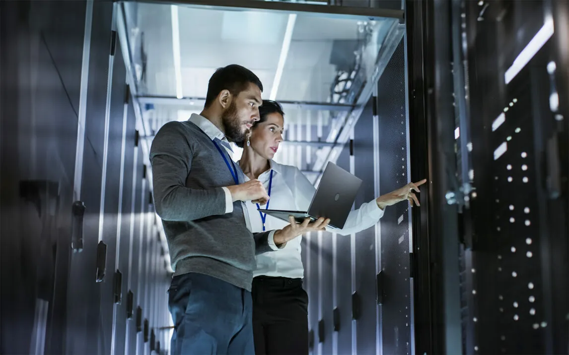 IT specialist with laptop talks to technician in the data center. IT specialist with laptop talks to technician in the data center.
