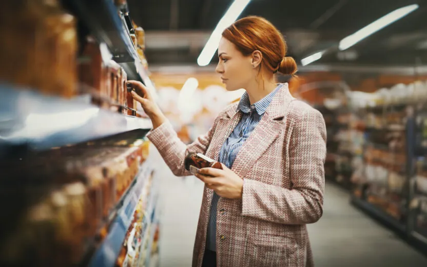 woman-holding-jar-in-supermarket-1095108328 Young woman holding a jar of Sun-dried tomatoes in supermarket. She's searching for specific manufacturer.