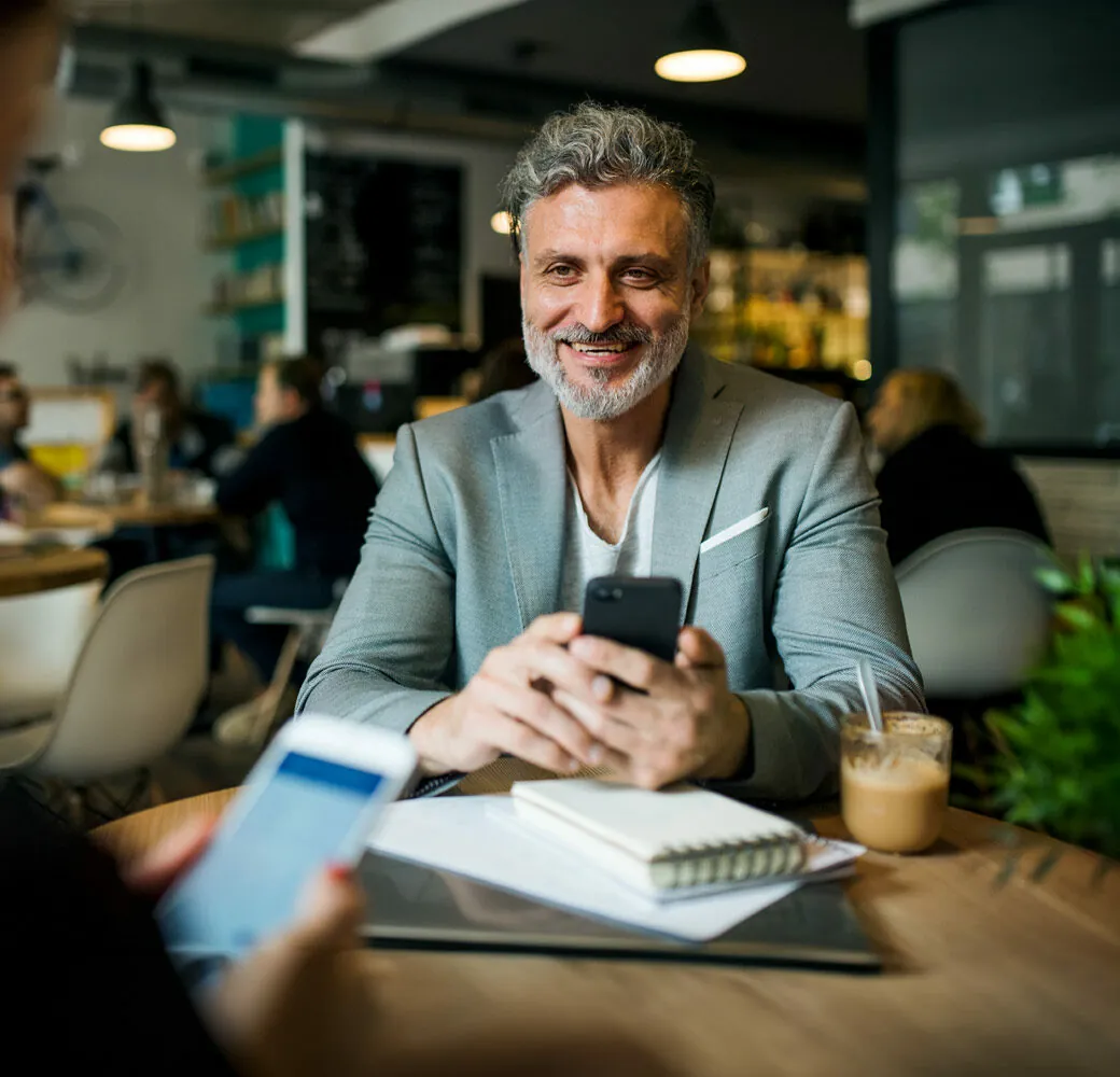 Man and unrecognizable woman having business meeting in a cafe, using smartphones.