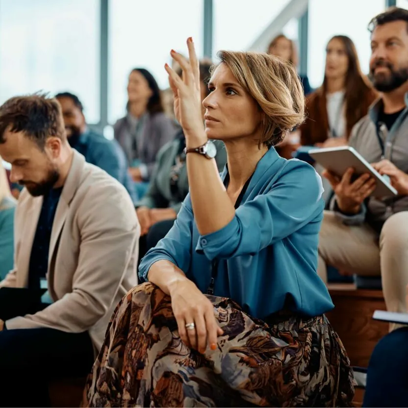Geschäftsfrau besucht ein seminar im konferenzsaal Eine Unternehmerin hebt ihre Hand, um eine Frage während einer Geschäftskonferenz im Kongresszentrum zu beantworten.