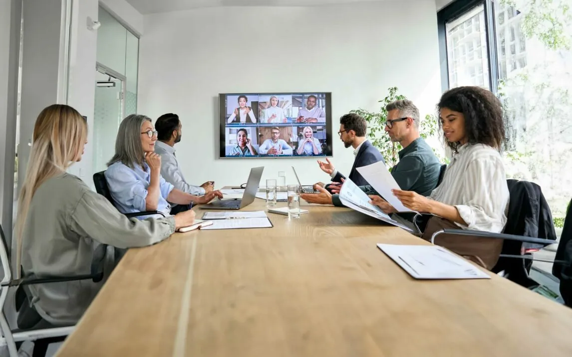 employees-on-online-conference-on-tv-screen-in-meeting-room-1333390966 Diverse company employees having online business conference video call on tv screen monitor in board meeting room. Videoconference presentation, global virtual group corporate training concept.
