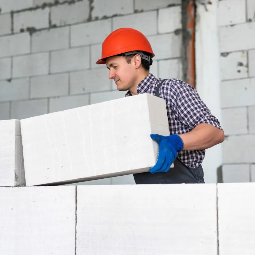 Man wearing a red helmet working, building a wall from bricks. Man wearing a red helmet working, building a wall from bricks.
