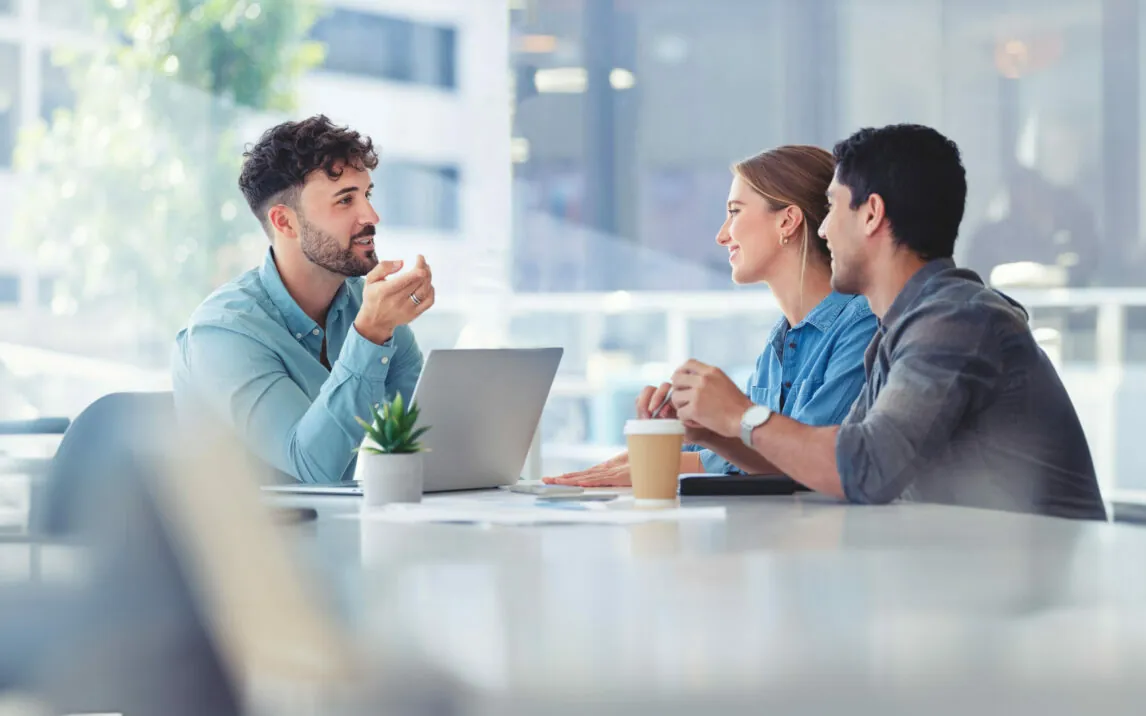 people-in-meeting-1334729682 People in a meeting, financial advisor with couple explaining options. The agent is using a computer. Couple are casually dressed. They sitting in an office and are discussing something with the agent.