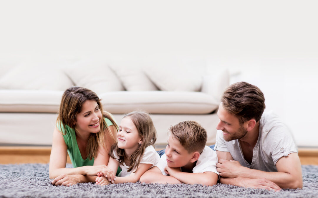 headerimage-boesch-family Bild von einem Paar ihren zwei Kindern auf einem flauschigen Teppich.