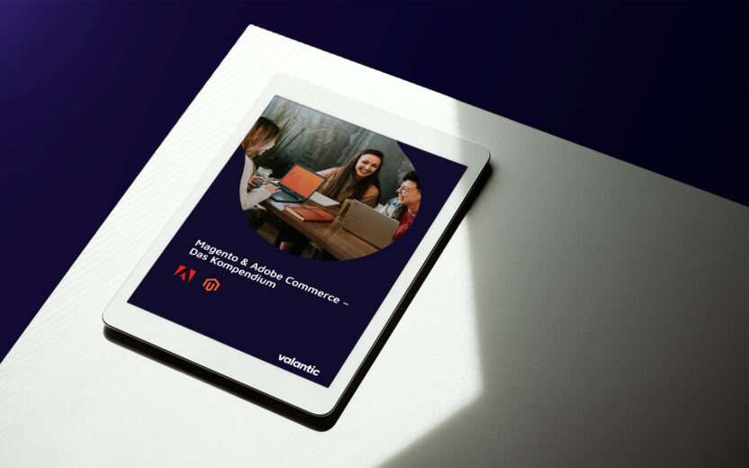 mockup-magento-business-kompendium Auf einem iPad wird ein Dokument mit dem Titel „Magento & Adobe Commerce – Das Kompendium“ auf einer hellen Oberfläche mit dunklem Hintergrund angezeigt. Das Dokumentcover enthält ein Gruppenfoto sowie Logos von Adobe und Magento.