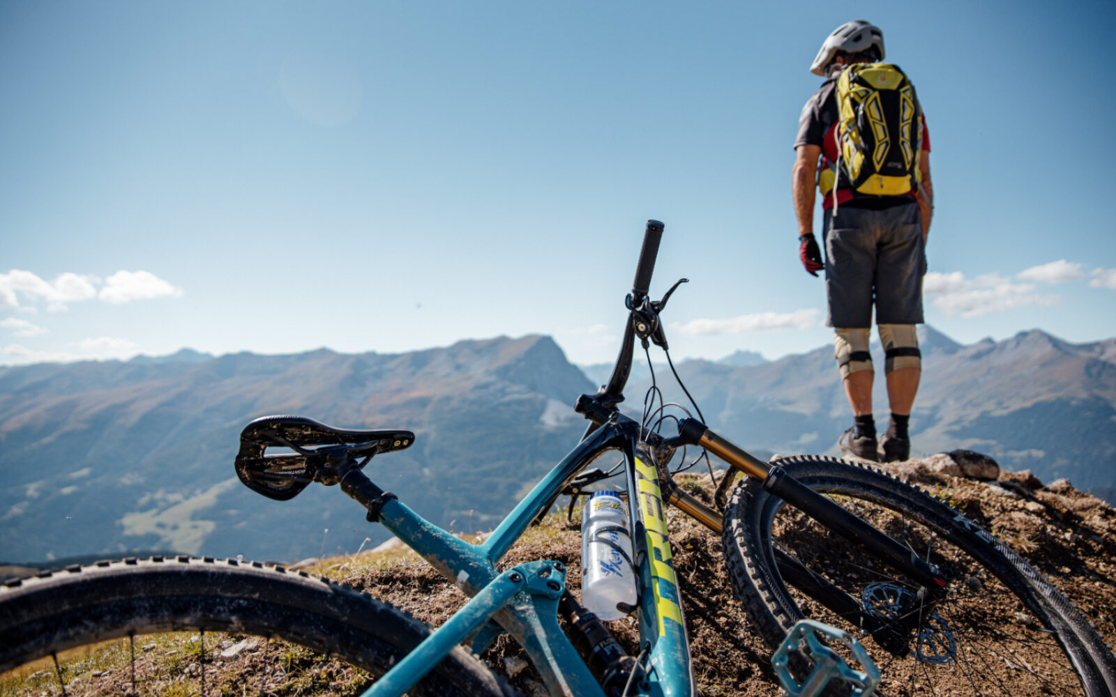 MTB-Holidays setzt auf Content Marketing von valantic Austria Bild von einem Mountainbike-Fahrer, der sein Fahrrad im vorderen Bereich des Bildes abgelegt hat & sich auf einen Felsen gestellt hat, von wo er ins Gebirge blickt.