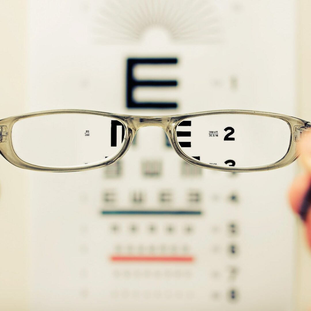 david-travis-aVvZJC0ynBQ-unsplash Eine Brille wird vor einem Sehtest-Textdokument gehalten, wodurch der Text durch die Gläser scharf und außerhalb der Gläser unscharf erscheint.