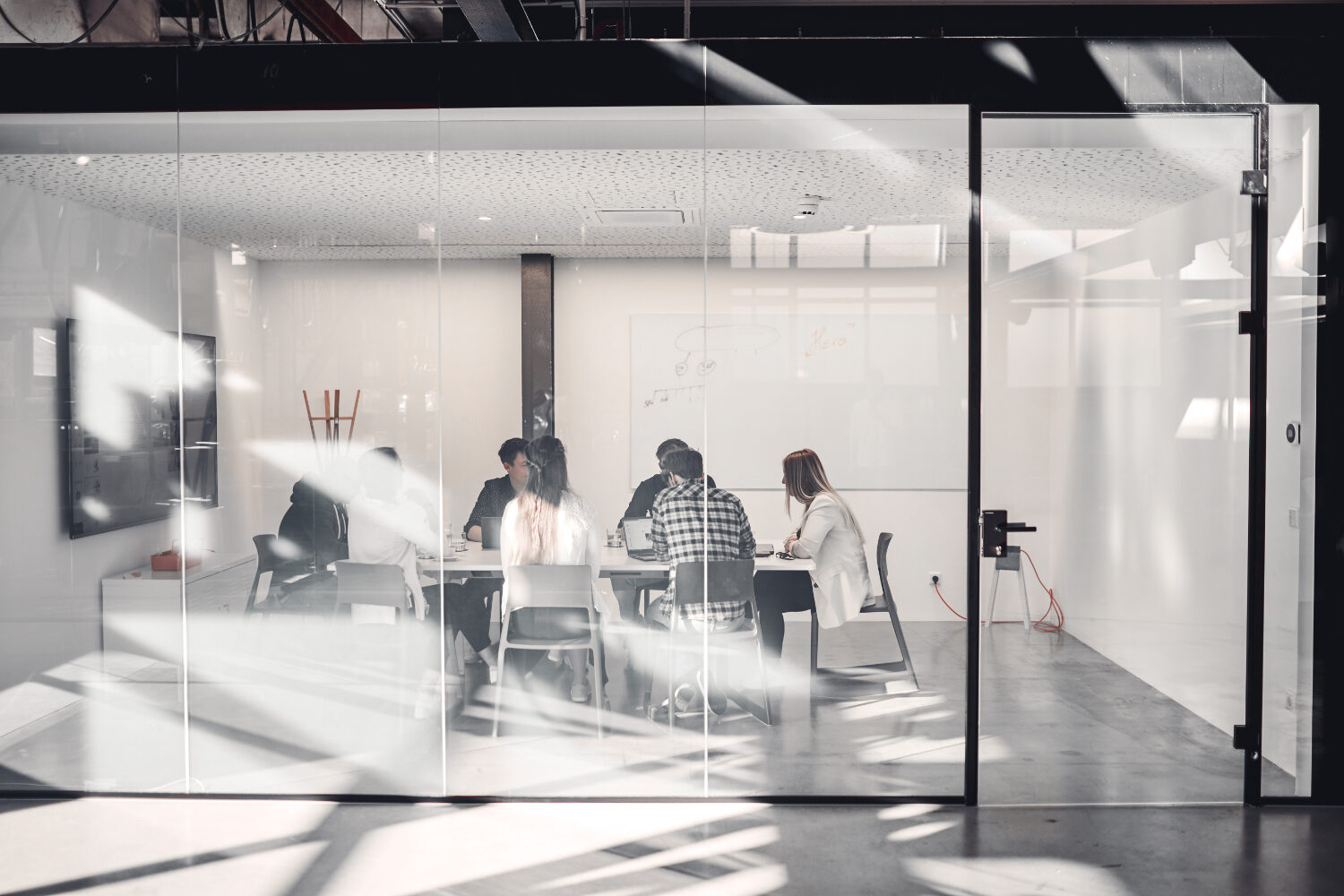 Langfristig erfolgreich durch Digital Identity Design valantic Austria Mitarbeiter*innen sitzen in einem verglasen Meeting-Raum und besprechen ein Projekt,