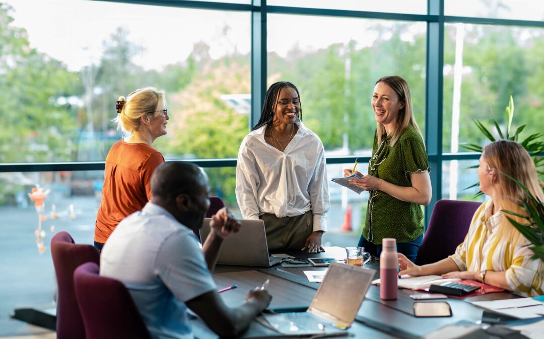 An over-the-shoulder view of a group of cheerful co-workers having a team briefing and enjoying some time away from their desks and recounting funny stories from the office. An over-the-shoulder view of a group of cheerful co-workers having a team briefing and enjoying some time away from their desks and recounting funny stories from the office.