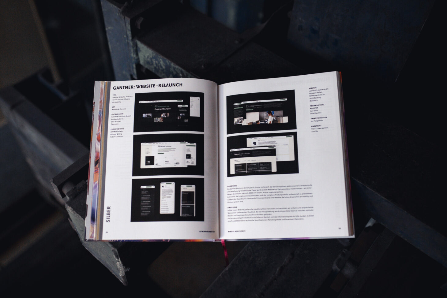Offenes Buch mit Seiten mit Informationen zum Website-Design, einschließlich Bildern von Webseiten und beschreibendem Text aus dem AMMA Jahrbuch 2025, platziert auf einer dunklen Oberfläche im Industriestil.