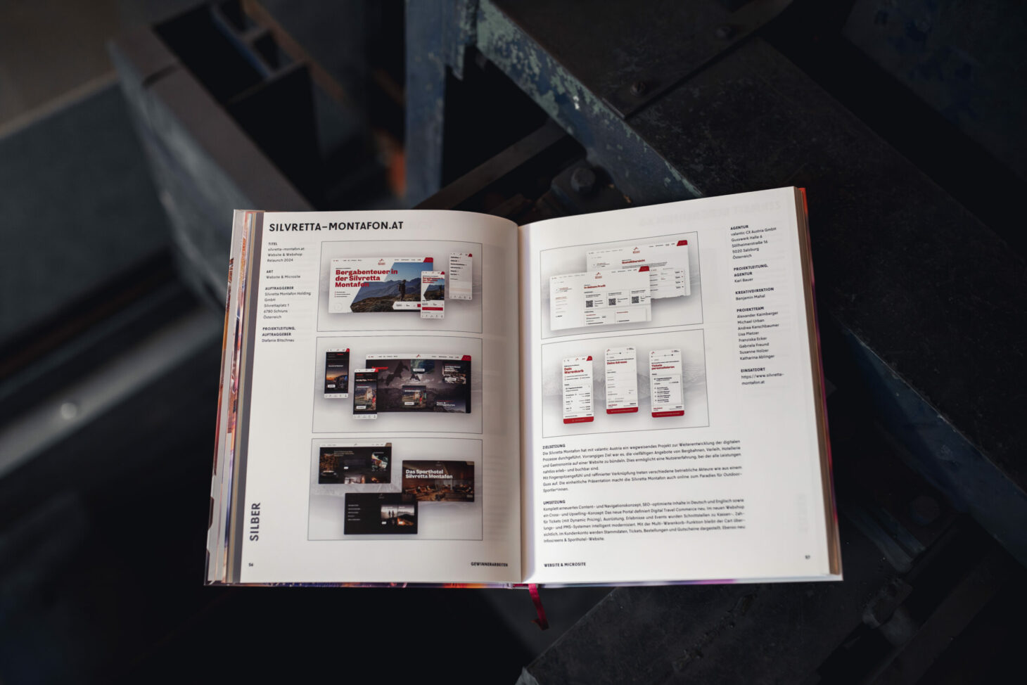 Auf einer dunklen Oberfläche liegt ein offenes Buch, dessen Seiten Website-Design-Layouts und Einblicke in das Projekt Silver Delta Montafon offenbaren, wie es im AMMA Jahrbuch 2025 vorgestellt wird.