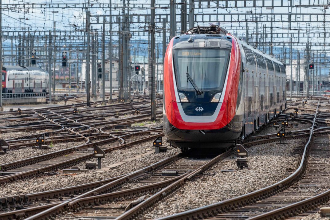 zug-schienenverkehr-sbb-zuerich Ein moderner rot-weißer SBB-Zug fährt auf einem komplexen Netz aus Gleisen mit Oberleitungen und integriert die RFID-Technologie effizient für einen reibungslosen Betrieb.