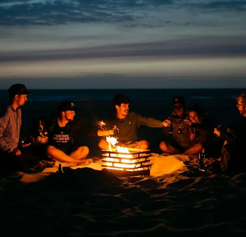 Eine Gruppe junger Leute sitzt bei Sonnenuntergang am Lagerfeuer mit dem Feuerkorb Cube von höfats.