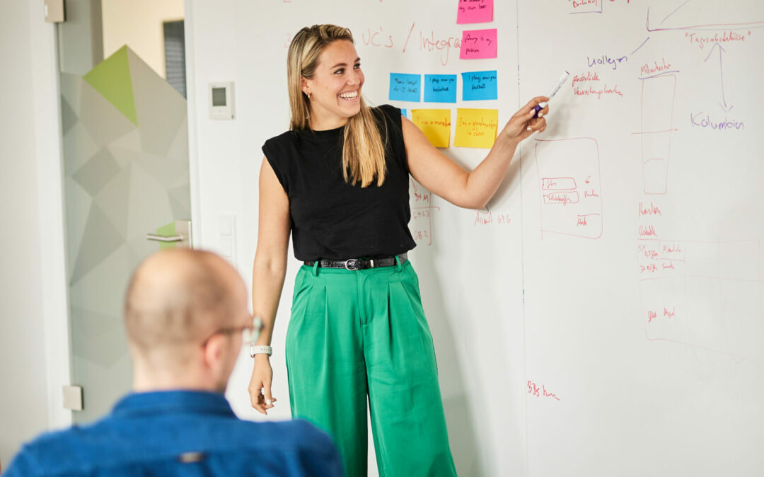 CX-Valantic_Langenfeld_0280 Foto von einer Frau, die an einem Whiteboard steht und ihren Kolleg*innen die neu Strategie erklärt.