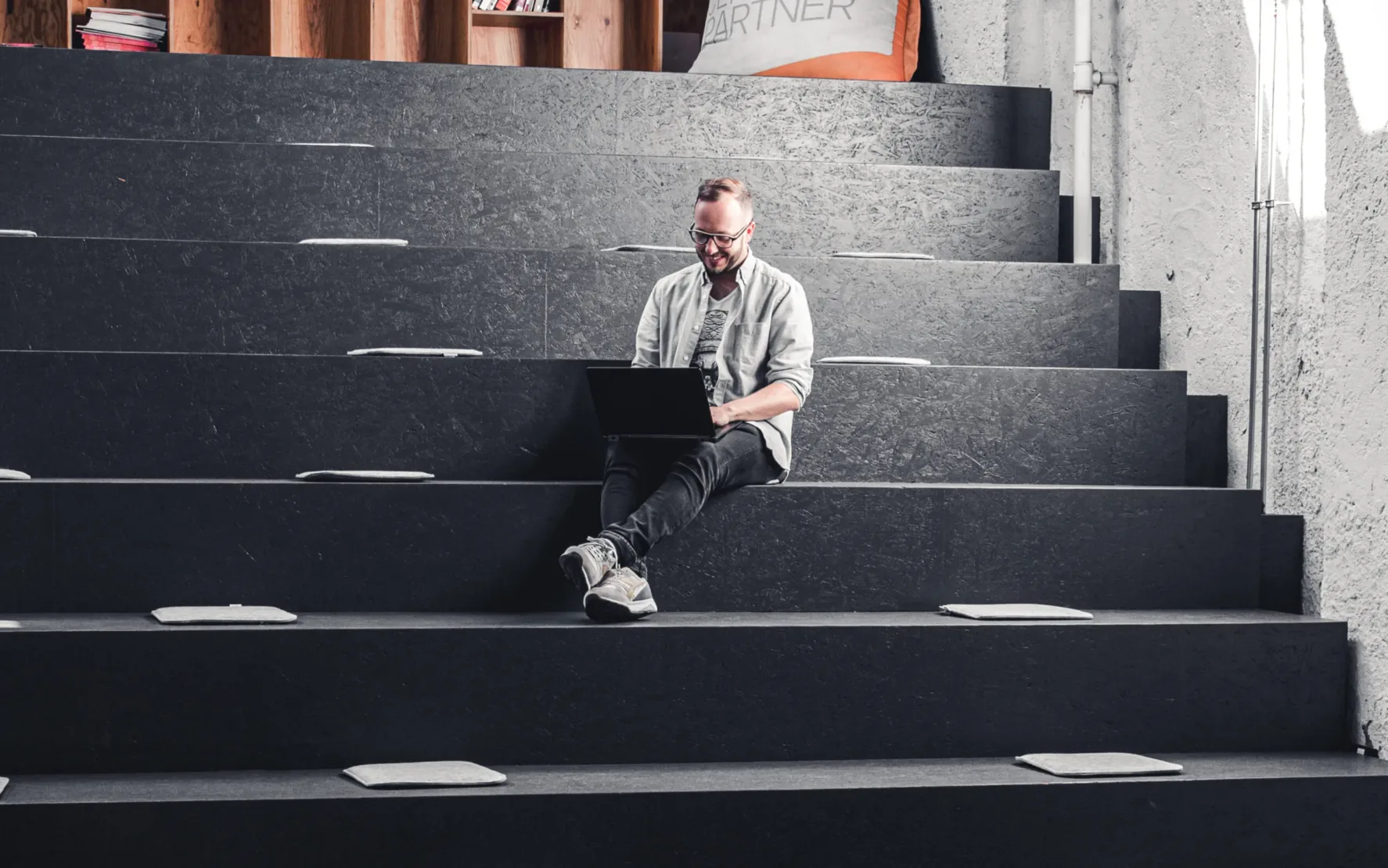 Pimcore ♥ valantic Austria Junger Mann, der auf einer großen Sitztreppe sitzt und mit einem Laptop am Schoß mit Pimcore arbeitet.