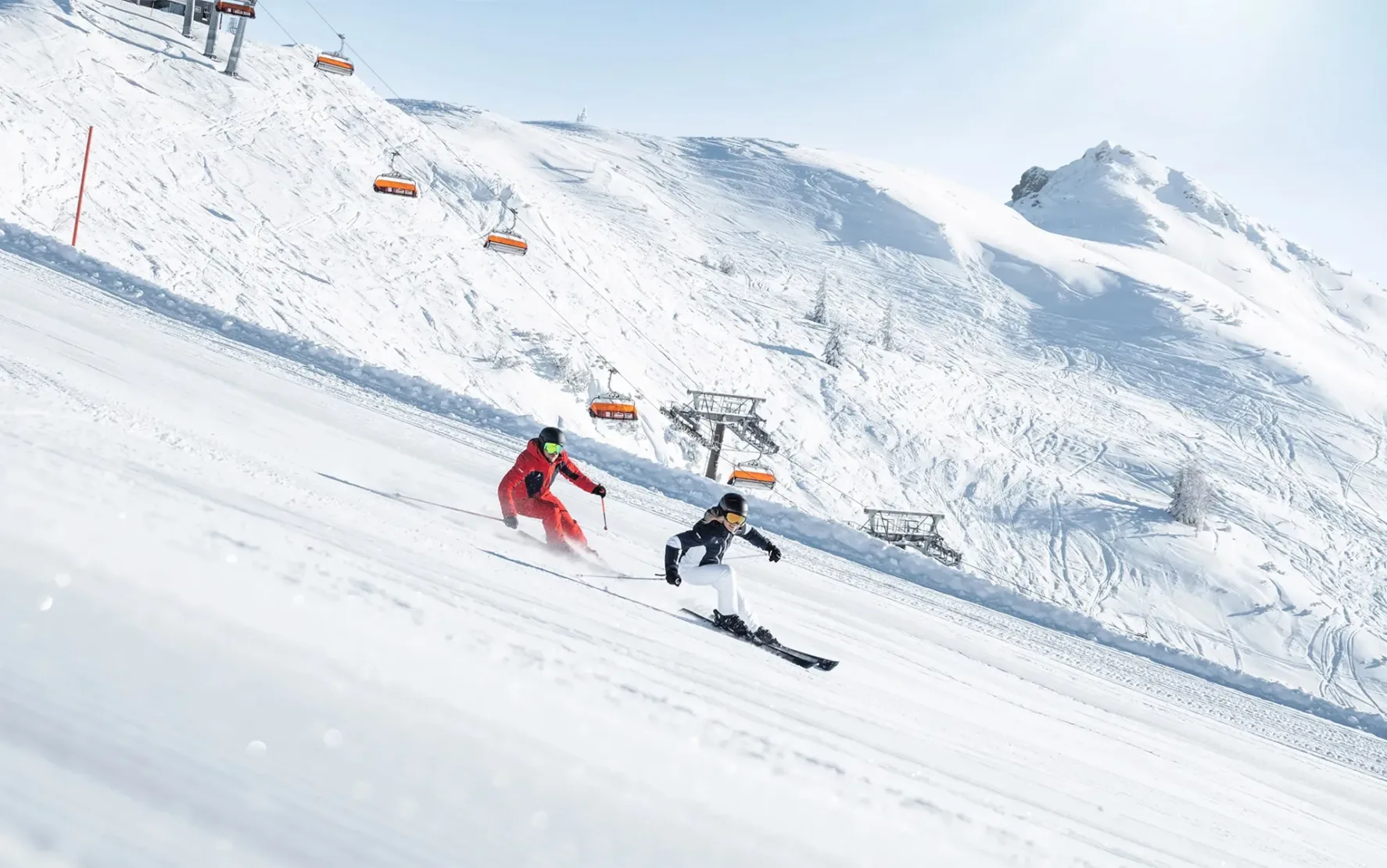 Ski amadé – Perfekte Pisten für unvergessliche Abfahrten Zwei Skifahrer in Aktion auf einer perfekt präparierten Piste mit Blick auf Skilifte und schneebedeckte Berge.