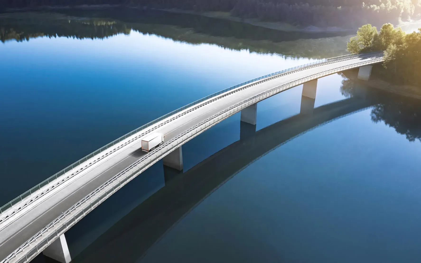 Die Eberspächer Gruppe schaltet durch die Zusammenarbeit mit valantic Austria einen Gang höher. Bild von einer großen Betonbrücke, die über strahlend blaues Wasser führt. Auf der Brücke fährt nur ein einzelner weißer Lkw. Am Rand kann man einen Wald erkennen.