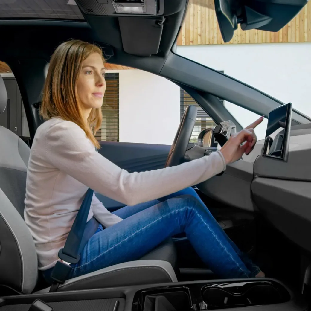 woman-sitting-in-car-1389670242 Side view of woman smiling and sitting while touching device screen in modern car.